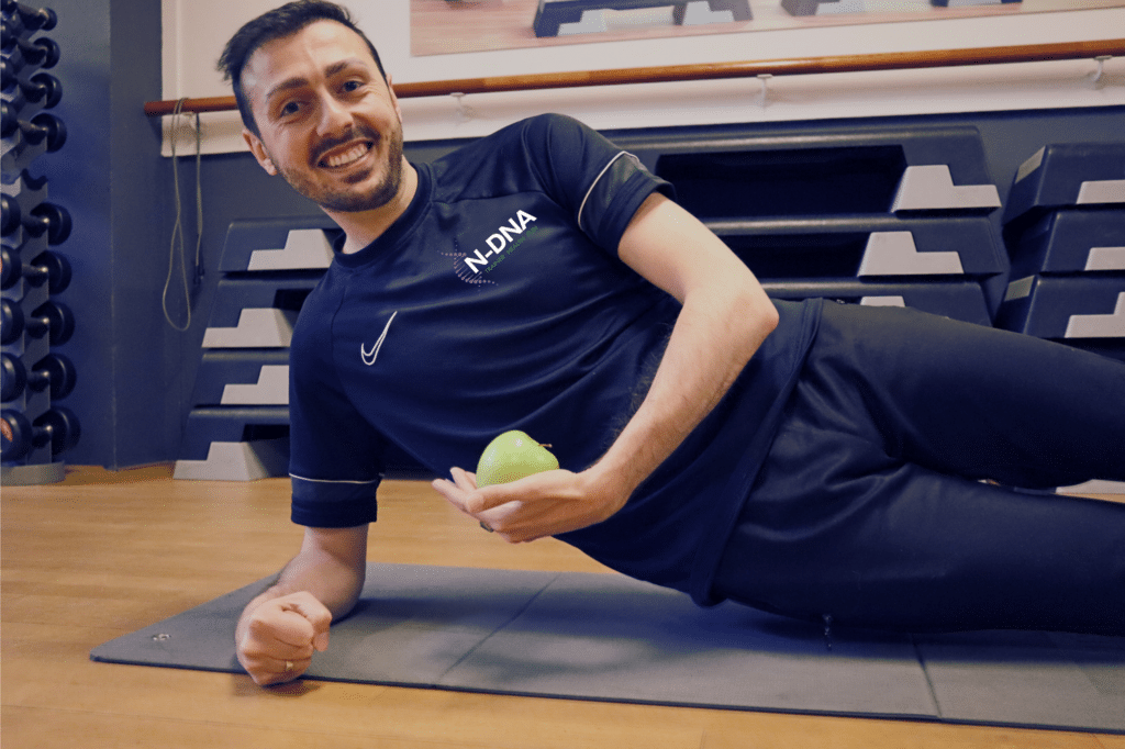 Nidjat Trainer ligt op een yoga mat met appel te poseren.
